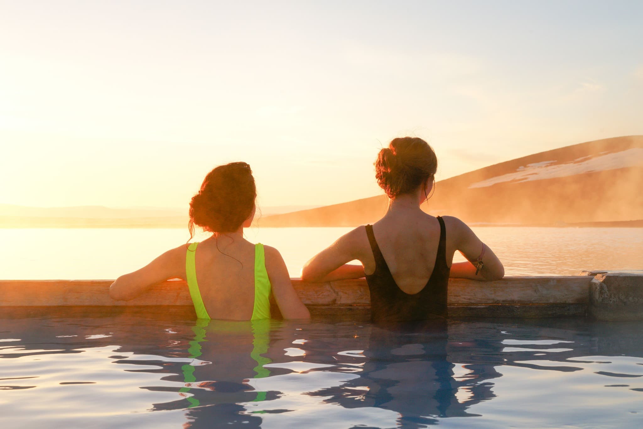 Two people relaxing in a warm outdoor pool overlooking a dramatic landscape
