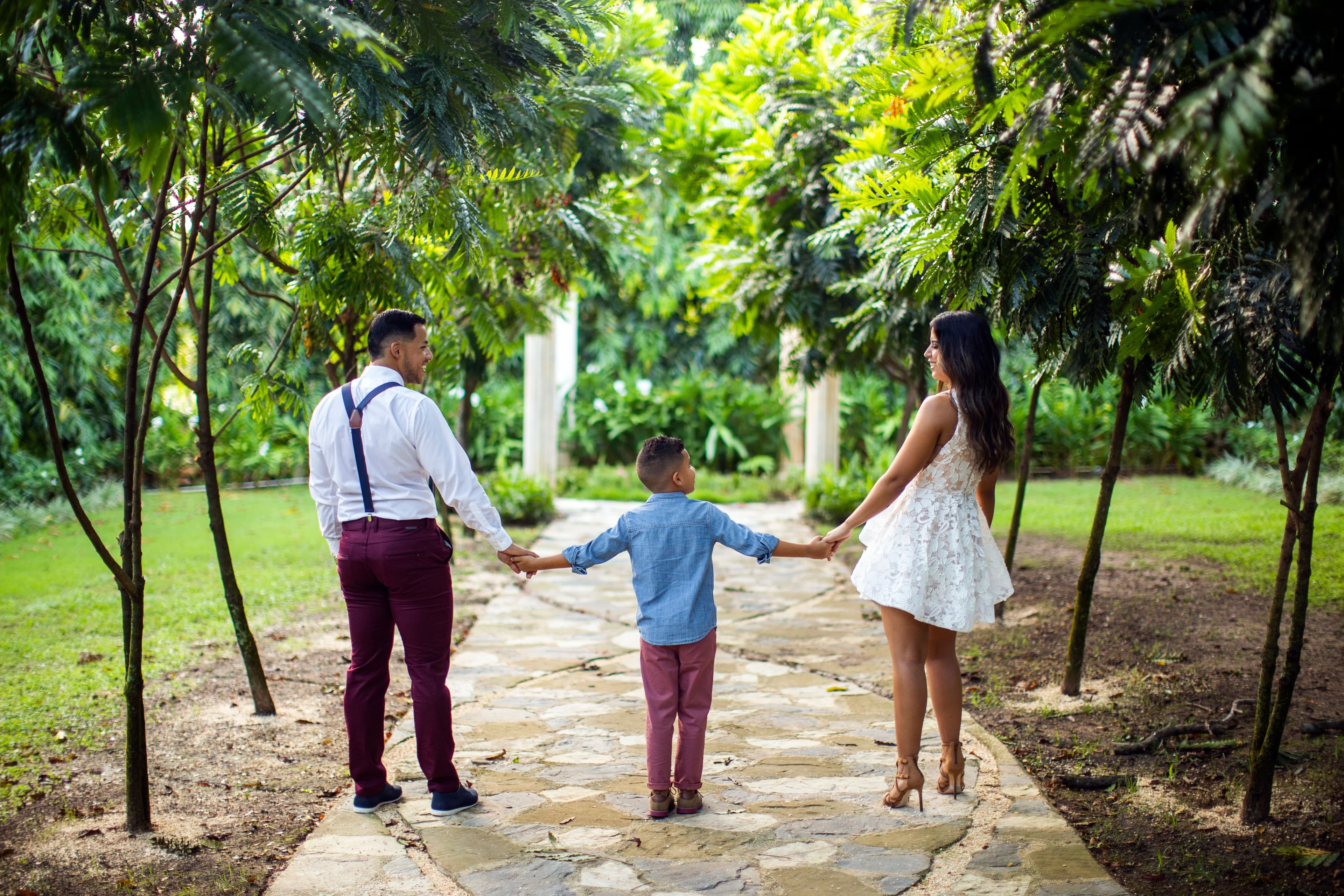 Parents walking hand in hand with their child through a garden