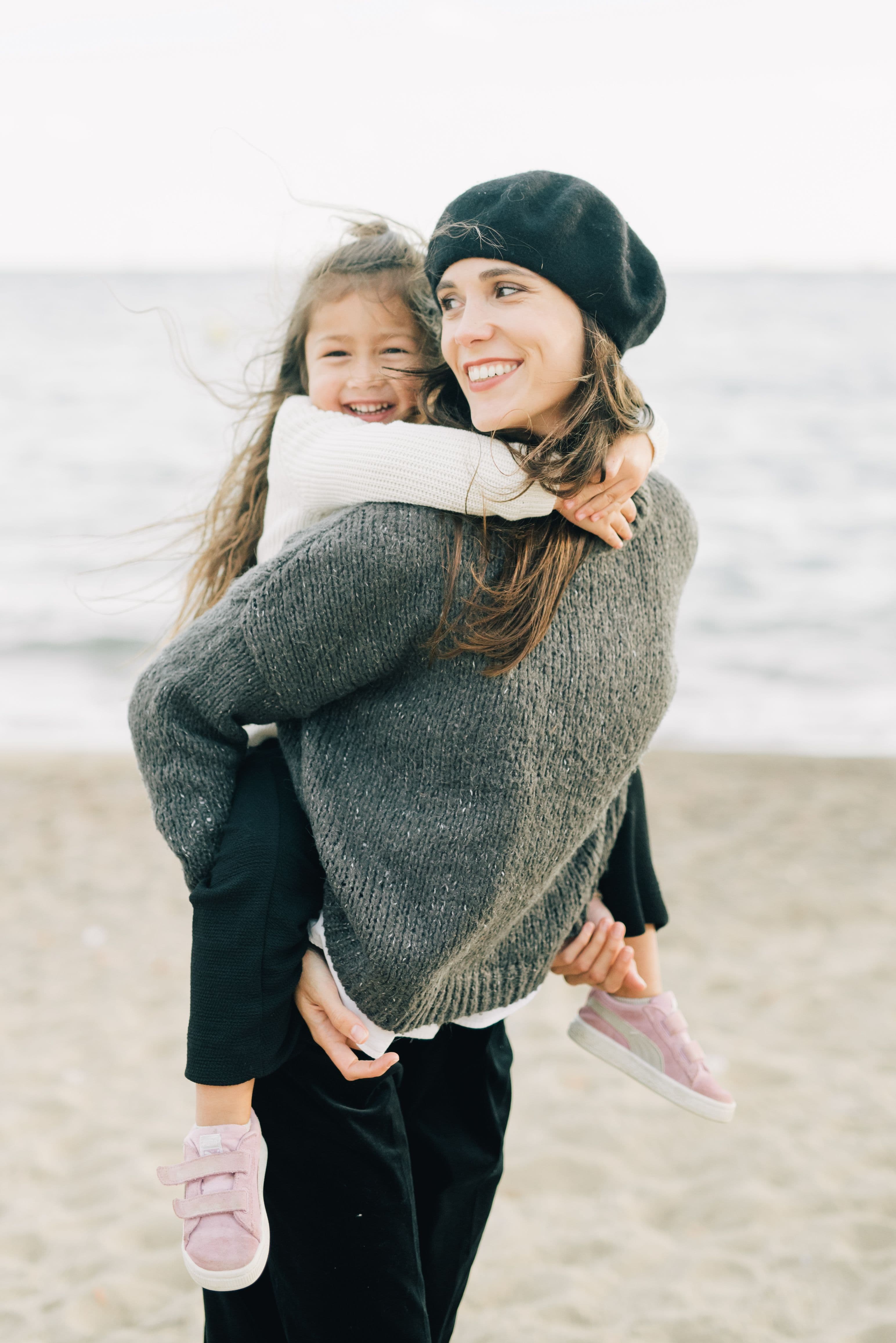 A mother carrying her smiling daughter by the sea